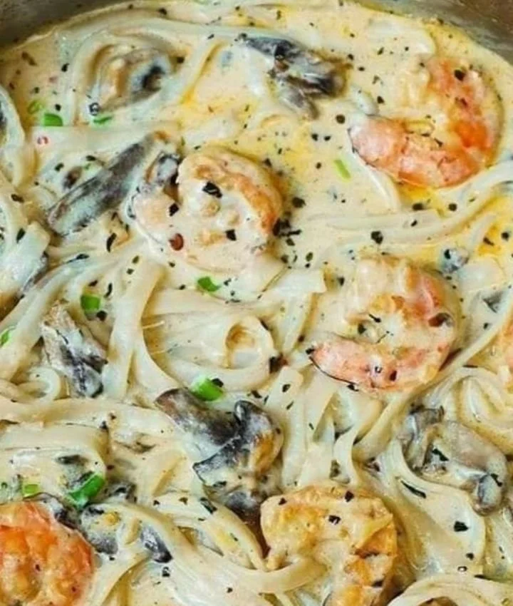 Prato de macarrão cremoso com camarão e cogumelos, preparado de forma deliciosa.